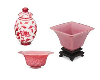 1051
20th century
A Group Of Chinese Peking Glass
Pink etched bowl marked to the underside with an apocryphal reign mark for Qianlong Period (1736-1795)
Comprising two pink glass bowls, one etched with a foliate and avian motif and one squared, set on a carved wood stand, along with a red and white cameo-style glass lidded jar with foliate and butterfly motifs, 4 pieces
Largest: 8.5" H x 4.25" Dia.; smallest: 3.5" H x 7.75" Dia.
Estimate: $300 - $500