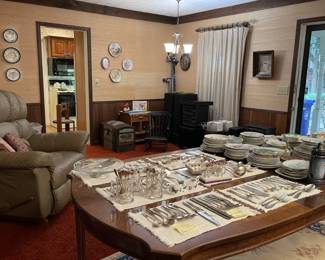 array of fine china, wood dining table, decorative plates, silverware, blue and beige area rug, leather recliner, child's rocking chair, framed wall  art, electronic audio equipment