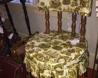 A sewing chair in a classic colonial pattern on vinyl. Next to it is a trio of leather attache’ cases. 
