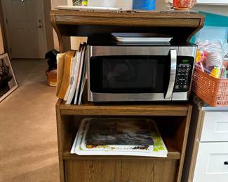 Microwave cart, microwave oven, variety of decorative cutting boards and cook books.