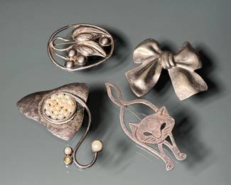 (4PC) STERLING SILVER PINS | Including a bow form pi (missing pin), a cat form pin, a pin mounted with pearls, and a pin with openwork leaf decoration; total weight 65.9g