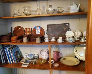 Lovely glass serving pieces and a teapot on top shelf, Gorgeous teak dish set with serving pieces. MCM coffee mugs, demitasse & tea cups and saucers, Travel books, Tile collection from Holland America, Blenko Daisy or Sunflower Bowl with tag, Wedgwood sand dollar plate, ceramic pitchers bowl and platter.