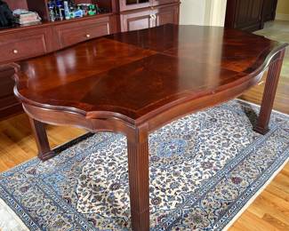 WINTERTHUR SHAPED TOP DINING TABLE | With center fields of reverse diamond matched flaming swirl-off-crotch-mahogany veneers, top separated by an inlay line of satinwood, ebony, and tulip-wood with a border of swirled mahogany veneer in a 90 degree orientation, raised over reeded legs with two 20” leaves and pads. -  l. 79 x w. 53 in 