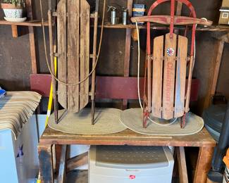 Plastic bench with storage, two vintage sleds, matching braided area rugs and work bench.