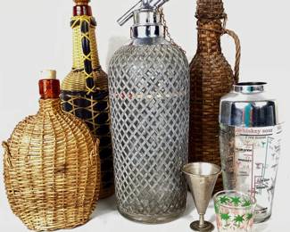 LIBE923 Vintage Art Deco Barware More 1930's art Deco Sparklets seltzer bottle with metal mesh casing, made in Czechoslovakia - missing nozzle cover. &nbsp;3 vintage liquor bottles encased in wicker. &nbsp;1 glass shaker - missing lid, flamingo shot glass, and metal gimlet.
