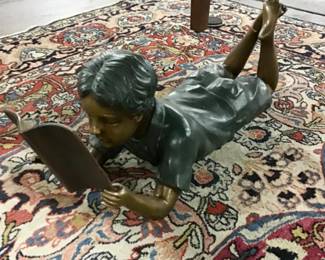 Bronze statue of a young boy laying down and reading a book.