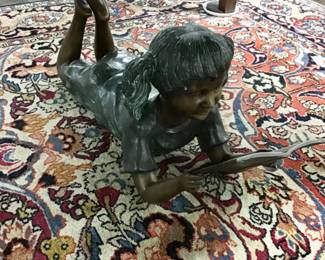 
Bronze statue of a young girl laying down and reading a book. 