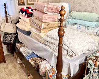 Full size 4 poster bed, and a table full of bedspreads, coverlets and blankets.
