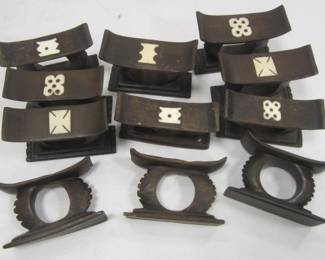 ELEVEN AFRICAN CARVED WOOD NAPKIN RINGS WITH INLAID DESIGNS ON THE TOP. MADE THE FORM OF AN AFRICAN HEAD REST