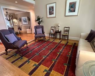 area rugs, silk flower arrangements, antique dining chairs, burgundy armchairs, beige sofa, throw pillows, brass and glass end table, framed wall art, display case, china cabinet