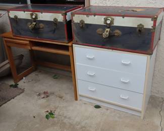 Two travel/storage trunks, old desk and white drawers.