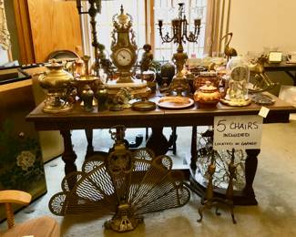 Heavy wooden antique dining table with chairs, many brass items.