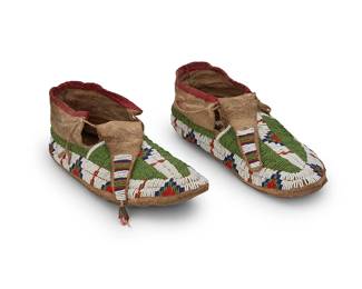 132
A Pair Of Cheyenne Beaded Hide Moccasins
Late 19th century; Southern Plains
Each beaded in green, blue, red, and white with geometric motif bands to sides center, with narrow beaded tongues with cone dangles, and each ankle edged in red plain weave fabric, 2 pieces
Each: 11-11.25" L x 3.25-3.5" H x 4-4.25" W approximately
Estimate: $500 - $700
