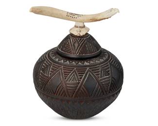 151
Steve T. Smith (B. 1948, Iroquois)
A lidded pot with antler finial, 1991
Incised to underside of pot: Talking Earth / STS / 91 / 3-847; incised to rim of lid: Talking Earth / STS / 91 / 3-840
The smoke kiln-fired lidded earthenware pottery vessel with allover incised geometric motifs; the lid with an incised, carved, and painted antler finial, one end carved in the shape of an eagle's head and inlaid with abalone eyes, surmounting a carved turtle figure base with a trim of applied shells
Pot: 5.875" H x 8.25" Dia.; lid: 5" H x 7.125" W x 4.625" D
Estimate: $300 - $500