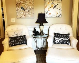 Matching white fabric armchairs with ottomans, black and white table lamps, glass side table