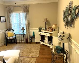 Matching white fabric armchairs with ottomans, black and white table lamps, glass side table, black dining chair, glass coffee table, black and white table lamp, large turquoise metal wall art