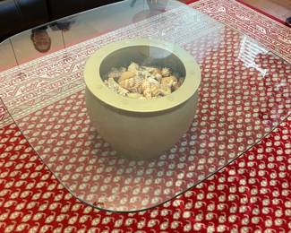 glass coffee table with large shell centerpiece, red and tan area rug