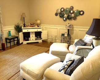 Matching white fabric armchairs with ottomans, black and white table lamps, glass side table, black dining chair, glass coffee table, black and white table lamp, large turquoise metal wall art