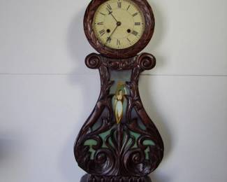 Lot 40:  Antique Walnut Banjo-Lyre Clock (This is a faithful copy of a 1830's Elmer Stennis Banjo-Lyre Clock) with floral & scroll carving over reverse painted glass panel, wreath carving around a Roman numeral dial, 8 day time and strike movement.  Early brass "swept wings" Eagle finial, 41 1/2" tall x 12 1/2" wide x 6" deep.  Cond:  Movement runs briefly. Minor Wear  Est. $200 - 400.