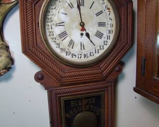 Lot 46: C/1890 Oak New Haven Calendar Regulator Clock, 30 day, time only, rope twist decoration around dial and lower drop, original brass pendulum and key, 18" x 4 1/2" x 33" h.  Cond: Original varnish has fine crazing, moderate dial wear on left side, running when photographed.   Est. $150 - 250.