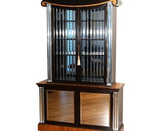 LORIN JACKSON ART DECO STEP-BACK CABINET | Circa 1935, Zebrawood and Philippine mahogany cabinet with lucite crown, spindle doors, and engaged columns, the lower case with mirrored glass panels, designed by Lorin Jackson for Grosfeld House. h. 87-1/2 w. 54 d. 16-3/4 in.
