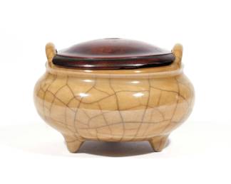 RARE CHINESE IMITATION 'BRONZE' PORCELAIN CENSER | Kangxi/Yongzheng reign (1662–1723), the porcelain tripod censer of Ge-type, having double handles over a squat bulbous body raised on three tapering feet in imitation of a Ming dynasty bronze form, covered in a 'bronze' colored glaze over a white body with characteristic Ge 'golden thread and iron line' crackle; base with recessed 'burnt' foot-rim; with conforming wooden lid. h. 3 dia. 4-3/4 in.