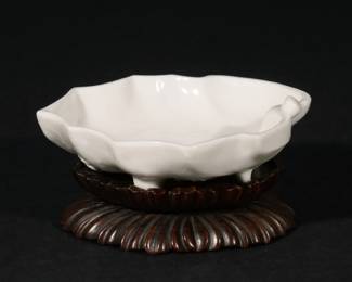 CHINESE DEHUA LEAF-FORM BRUSH WASHER | Late Ming - Early Qing dynasty, 17th-18th century, a shallow dish molded in the form of a leaf, with slightly incised ribs on interior, and flowering branches curling underneath the exterior to form the foot, wood stand
w. 5 in.