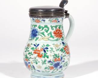 CHINESE WUCAI PORCELAIN JUG | Kangxi period, an export piece in the form of a jug or stein with single handle, decorated with floral designs in underglaze blue and overglaze enamels in green, yellow, and copper red, with conforming silver lid. h. 6-3/4 in.