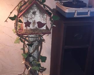 A rustic birdhouse sits atop vines with twinkling lights that work. Don’t miss the vintage portable record player on the right. 