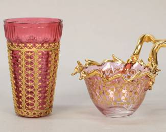 41	2 Pieces of Moser Style Glass	2 pieces of cranberry glass, possibly Moser. Cranberry cordial, with gilt metal overlay, 3 3/4"H; cranberry tea cup, with gilt enamel decoration and gilt decorated rim and handle, 3"H at handle. Both unsigned. Cordial scratches to the underside, tea cup flea bites to the underside, crack from handle into bowl of cup.
