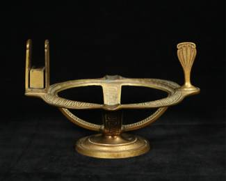 231	Tiffany Studios Etruscan Match Stand	Tiffany Studios gilt bronze match stand, in the Etruscan pattern. With match book holder and pipe tamper / snuffer. Center bowl missing. Stamped on the underside of the rim Tiffany Studios New York 2068. 8 1/8"W x 5 1/4"H. Some tarnishing to gilt bronze patina.
