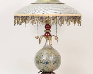 436	Luna Bella Table Lamp	Luna Bella table lamp. Patinated metal, blown glass center, foliate motif, metal shade with beaded fringe. 26"H to top of finial. Chips to finial, losses to patina on top of cap, losses to patina on base and feet.

