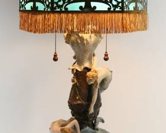441	Art Nouveau Mermaid Slag Glass Lamp	Art nouveau figural lamp with a slag glass shade. Painted metal lamp base with mermaids, lobster and fish. With a caramel and blue hexagonal slag glass shade, with brass overlay and fringed rim. Lamp base and shade both unsigned. 35 1/4"H to top of shade. Missing finial, lamp base appears to have been repainted, paint loss and crazing throughout base, later hardware appears to have been added to shade, minor chips and roughness to slag glass panels on interior of shade, losses to patina on brass throughout shade.
