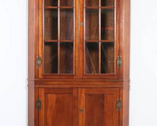 287	Federal Style Corner Cabinet	"Federal style corner cabinet. 21st century. Two glazed doors concealing two shelves, lower doors concealing one shelf, brass hardware. Light scuffs and wear to interior. Small chips and scuffs to wood along front left and right edges. Two holes to wood on back paneling on lower section of cabinet. Key is not included.
37 1/2"" W x 21"" D x 80 1/2"" H. 97 lbs."
