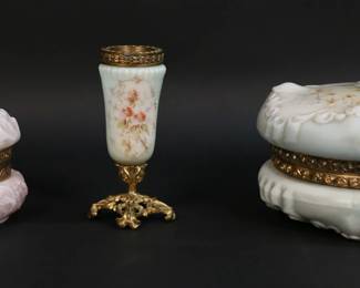 27	3 Pieces Wave Crest Glass	3 pieces Wavecrest. Opaque glass, gilt metal mounts, hand painted decoration. Round dresser box with cherub decoration, unsigned, 3 5/8"H x 7 1/8"-diameter; small dresser box, 3 1/4"H x 4 1/4"-diameter, Wave Crest Trade Mark; bud vase, unsigned, 5"H. Larger dresser box scratches to underside, some losses to color on body of box.
