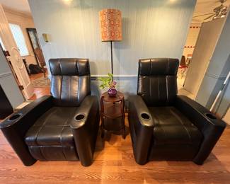 Family Room-Main Floor: Two black recliners with cup holders are separately priced. The next photo shows the side of one of them which still has its original tag attached. The floor lamp with geometric shade and the small three-tier table are also for sale.