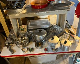 Vintage pots and pans, cookie cutters, bakeware and ice cream scoop all displayed on a antique enamel top table.