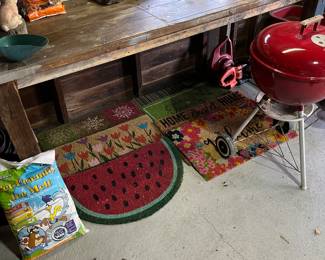 Work bench, Weber charcoal grill, variety of welcome mats, rock salt, ceramic planters and lawn/garden tools.