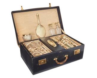 15
An Art Deco Gold And Glass Vanity Set, Cartier
Each piece with Chinese style font monogram, comprising 3 brushes, each with silk bristle guard bands, 1 hand mirror, 1 shoe horn, 1 nail file, 1 nail buffer and case, 1 box, 1 button hook, 2 silver gilt manicure scissors, 1 comb handle, 1 powder puff and powder jar, 8 various jars, two perfume bottles with daubers, and a small oval tray, all housed in a blue leather handled case with brass hardware, with canvas cover, with a two-level fitted moiré silk taffeta-lined interior, 25 pieces, Each item except scissors marked for 14K gold; scissors marked 14K and STERLING, blades marked 'WB KERR GERMANY'; each further marked: G 1900 BO or D 4270 BO Cartier, circa 1920s.
Case: 8" H x 24 1/2" W x 16" D; mirror: 12 1/8" H x 5" W x 1/3" D
Estimate: $30,000 - $50,000