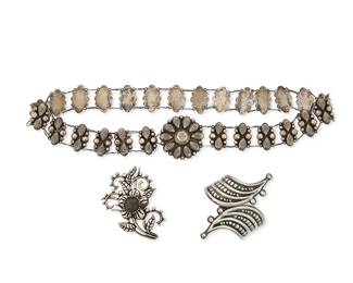 2235
A Group Of Mexican Silver Jewelry
Mid/late 20th century
Three works:

A sterling silver chain link belt with backed repoussé floral buckle and petal and ball links
Stamped: AM [in triangle] / Sterling / 925 / GUAD / Mex__ / R. _[S?]
30.5" L x 2" H

A Doris silver floral brooch with inset stone
Stamped: Doris / Silver / Corpus Artisans / Mexico
3.5" H x 2.375" W

A sterling silver pointed swirl crossover hinged cuff bracelet with silver ball accents
Stamped: TA-164 / Mexico / 925
6.75" inner C x 3.625" H

3 pieces
179.8 grams gross
Estimate: $300 - $500