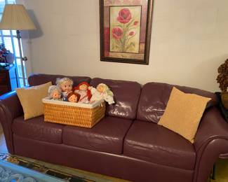 Plum leather couch. Basket of dolls - cricket, vintage strawberry short cake & cabbage patch kids