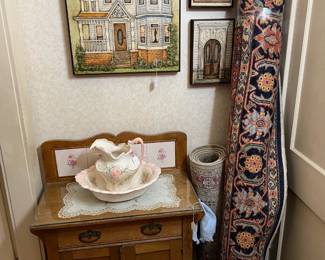 Three framed artworks are here, along with two rugs (one is peeking out from behind the other) and a side table with pitcher and wash basin.