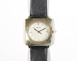 TIFFANY & CO. / UNIVERSAL 18K GOLD SQUARE CASE WRISTWATCH | Silver dial with baton numeral markers, square 18k gold case the interior marked "UNIVERSAL / GENEVE / .750" with quartz movement; case 29 mm, strap 8.25 in., 25.9g total weight
