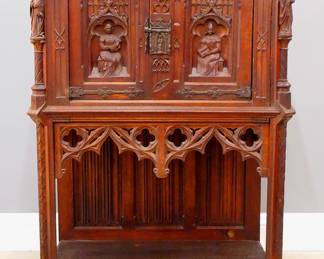 A turn of the century Gothic Revival Period carved Oak court cupboard.  Molded top with canted corners over two doors with carved tracery and figural panels, rope twist columns surmounted by carved Apostles, over an open lower shelf with linen fold carved back panel, Iron hinges and figural Apostle lock.  Original finish with some wear, damage and shrinkage, lacks piece of pierced skirt at side.  37 x 21 1/4 x 53" high overall.