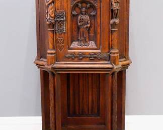 A turn of the century Gothic Revival Period carved Oak side cupboard.  Molded top with canted corners over one central door with carved tracery and figural panel, rope twist columns surmounted by carved Apostles, over an open lower shelf with linen fold carved back panel, Iron hinges and lock.  Old finish with some wear, minor damage and shrinkage.  25 x 17 1/4 x 48 1/2" high overall.