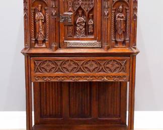 A turn of the century Gothic Revival Period carved Oak court cupboard.  Molded top over one central door with carved tracery and figural panel, flanked by carved spires and figural panels, over an open lower shelf with linen fold carved back panel, Iron hinges and lock.  Original finish with some wear and shrinkage.  38 x 20 1/2 x 58 3/4" high overall.