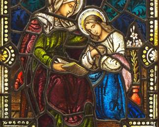 A Gothic Revival stained glass window of St. Anne and the Virgin Mary.  Multi-color stained and leaded glass panels with reverse painted detail depicting St. Anne teaching a young Virgin Mary to read within geometric and foliate borders.  Both face panels cracked, some wear to paint.  In a later Oak frame, 19 x 28" high overall.