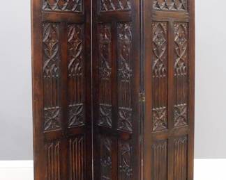A turn of the century Gothic Revival Period carved Oak dressing screen.  Three panel screen with carved trefoil crown above a quatrefoil frieze and tracery panels flanking a central carved shield and lower linen fold carved panels.  Older finish with some wear and flaking.  Each panel is 18 x 63 1/2" high, 54 x 63 1/2" high overall.