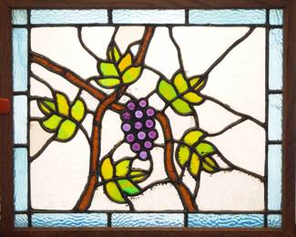 A turn of the century American stained glass window.  Multi-color stained and leaded glass panels depicting a scrolling Grape Vine design with faceted and textured glass accents.  One cracked panel at border.  In an Oak frame with minor wear, 22 1/4 x 18 1/2" high overall.