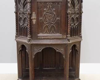 A turn of the century Gothic Revival Period carved Oak court cupboard.  Molded top with canted corners over one central door with carved tracery, rope twist columns surmounted by carved Apostles, over an open lower shelf with linen fold carved back panel, Iron hinges and lock.  Original dark finish with wear and some damage.  35 1/2 x 19 1/4 x 54 1/4" high overall.